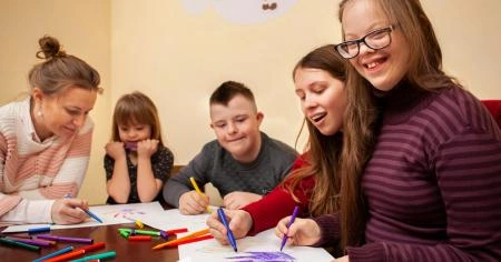 garota feliz com síndrome de down posando enquanto desenha com amigos e professora